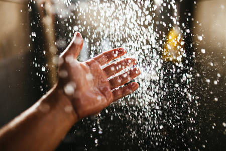 A mans hand in a spray of water in the sunlight against a dark background. Water as a symbol of...