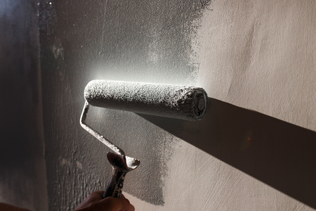 Home repairs. Painting the walls of the room in gray with a paint rollerの写真素材