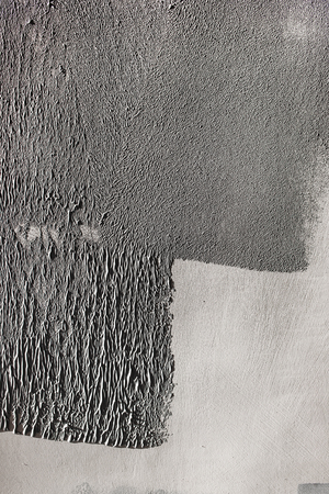 Concrete wall partially painted in gray with a paint roller. Paint texture in side sunlight