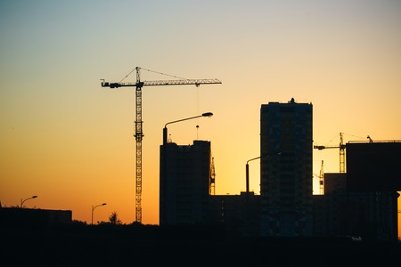 Silhouette of construction cranes over new residential buildings at sunset. Urban background