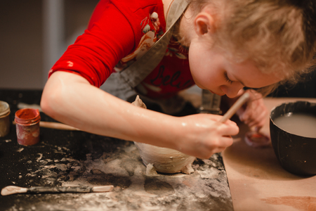 Young seven years old girl in pottery workshop creating a bowl from clay. Pottery workshop for kidsの写真素材