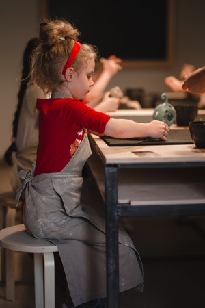 Young seven years old girl in pottery workshop creating a bowl from clay. Pottery workshop for kids