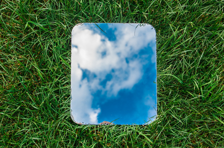 Rectangular mirror reflecting the blue sky with clouds lying on the green grassの写真素材