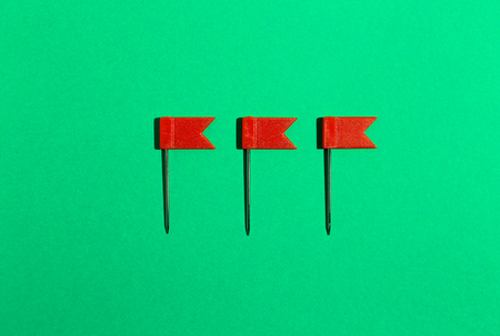 Three red little flag pins on a green background. View from above
