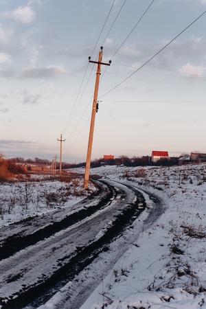Country dirt road with muddy puddles and melting snow in early spring at sunsetの写真素材