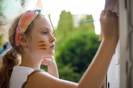 Girl paints a cardboard house at summer day, outdoor