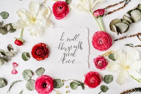 Phrase "Do small things with great love" written in calligraphy style on paper with pink, red roses, ranunculus,   white flowers and green leaves isolated on white background. Flat lay, top viewの写真素材