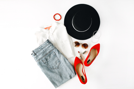 flat lay feminini clothes and accessories collage with blouse, jeans, sunglasses, bracelet, lipstick, red high heel shoes, earrings and hat on white background.