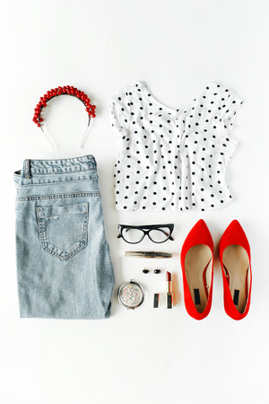 flat lay feminine clothes and accessories collage with shirt, jeans, glasses, mascara, lipstick, red high heel shoes, earrings and hoop on white background.の写真素材