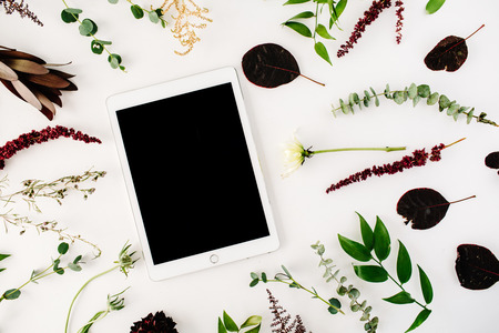 creative decorated and arranged flat lay frame concept with tablet, green and purple branches on white background. top viewの写真素材