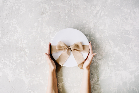 white gift cardboard box with brown bow and girl's hands on concrete background. flat lat, top viewの写真素材