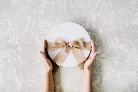 white gift cardboard box with brown bow and girl's hands on concrete background. flat lat, top viewの写真素材