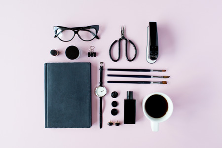 Flat lay, top view black style office table desk. feminine working supplies: glasses, diary, watches, perfume, brushes, scissors, coffee on pink background.の写真素材