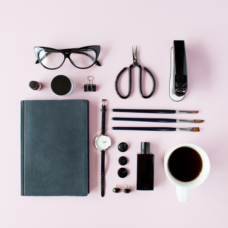 Flat lay, top view black style office table desk. feminine working supplies: glasses, diary, watches, perfume, brushes, scissors, coffee on pink background.の写真素材