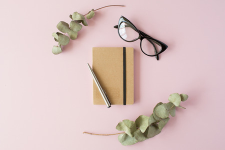 craft diary, pen, green leaves and glasses on pink background. Flat lay, top viewの写真素材