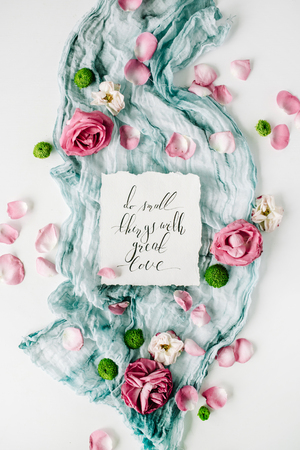 inspirational quote written in calligraphy style on paper with red roses, pink petals and blue textile on white background. Flat lay, top viewの写真素材