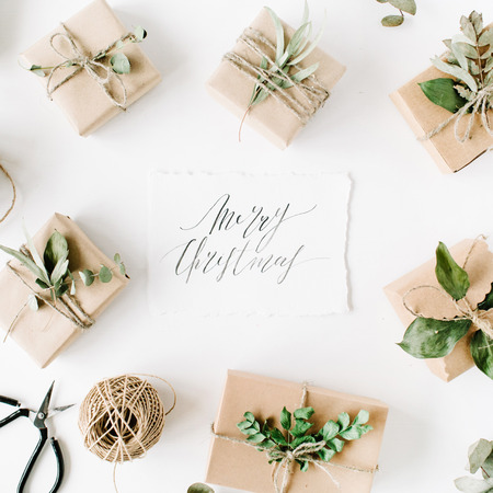 calligraphy words merry christmas and beauty arrangement frame of craft boxes and green branches on white background. flat lay, top viewの写真素材