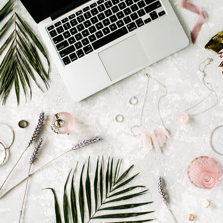 flat lay feminine home office workspace with laptop, proteus flower, necklace, palm branches and accessories. top viewの写真素材