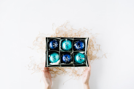 female hands holding box with bright blue christmas balls on white background. flat lay, top viewの写真素材
