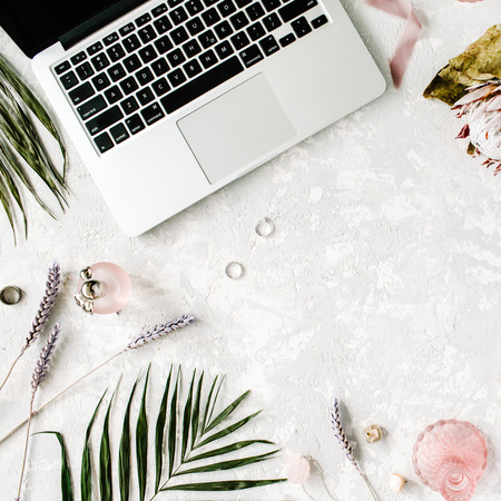 flat lay feminine home office workspace with laptop, proteus flower, necklace, palm branches and accessories. top viewの写真素材