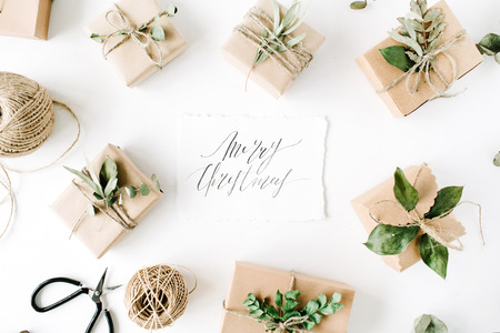 calligraphy words merry christmas and beauty arrangement frame of craft boxes and green branches on white background. flat lay, top viewの写真素材