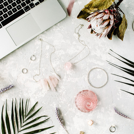 flat lay feminine home office workspace with laptop, proteus flower, necklace, palm branches and accessories. top viewの写真素材