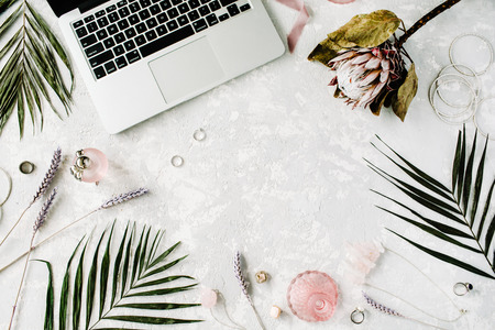 flat lay feminine home office workspace with laptop, proteus flower, necklace, palm branches and accessories. top viewの写真素材