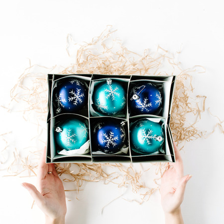 female hands holding box with bright blue christmas balls on white background. flat lay, top viewの写真素材