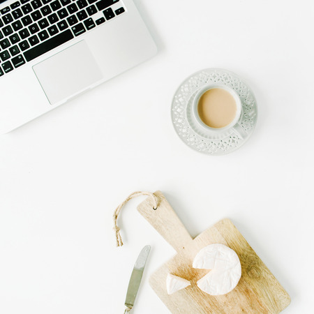 Flat lay modern feminine home office workspace. Laptop, coffee cup, cheese and knife on white background. Top viewの写真素材