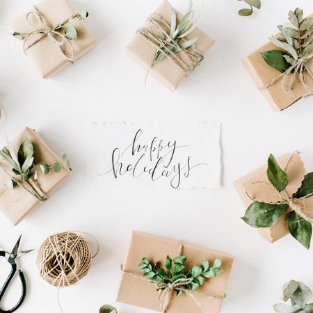 calligraphy words happy holidays and beauty arrangement frame of craft boxes and green branches on white background. flat lay, top viewの写真素材