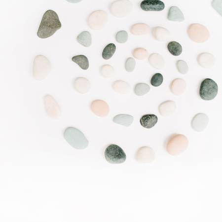 Creative spiral arrangement of colored stones. Mint, pink, beige and grey stones on white. Flat lay, top viewの写真素材