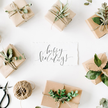calligraphy words happy holidays and beauty arrangement frame of craft boxes and green branches on white background. flat lay, top viewの写真素材