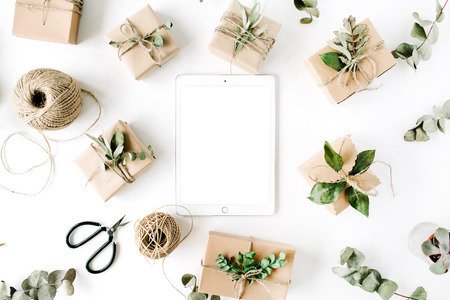tablet with mock up screen and beauty arrangement frame of craft boxes and green branches on white background. flat lay, top viewの写真素材