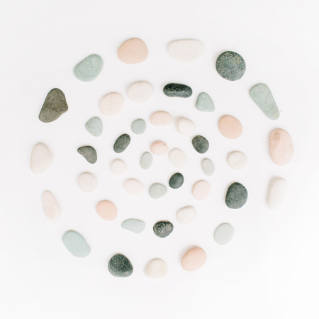 Creative spiral arrangement of colored stones. Mint, pink, beige and grey stones on white. Flat lay, top viewの写真素材