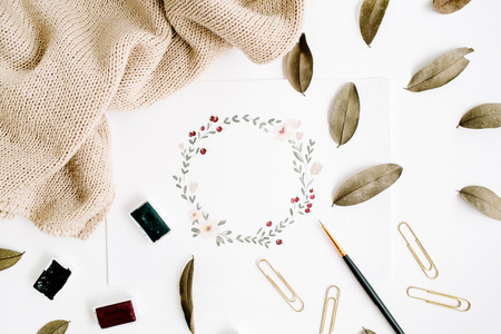 Artist workspace. Floral wreath frame painted with watercolor, paintbrushes, dried leaves, pullover. Flat lay, top viewの写真素材