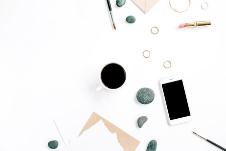 Home office workspace with coffee, mobile phone, craft envelope, stones, headphones and paper blank on white background. Flat lay, top view.の写真素材