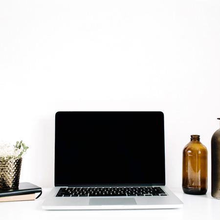 Blogger or freelancer workspace with front view of laptop with black blank screen at white background. Minimalistic decorated home office desk.の写真素材