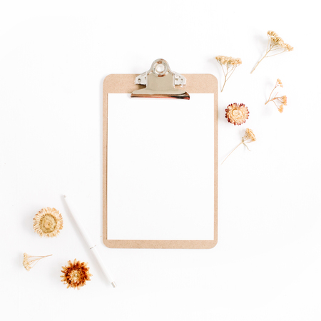 Clipboard mock up and pale dried flowers on white background. Flat lay, top view minimalistic brown styled home office desk. Beauty blog concept.の写真素材