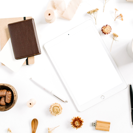 Blogger or freelancer workspace with tablet, coffee mug, notebook, sweets and accessories on white background. Flat lay, top view minimalistic brown styled home office desk. Beauty blog concept.の写真素材