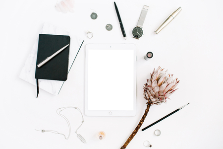 Blogger or freelancer workspace with blank screen tablet, protea flower, notebook, watches and feminine accessories on white background. Flat lay, top view minimalistic decorated home office desk.の写真素材