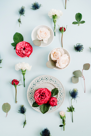 Flowers pattern made of red and beige roses on plate, white carnation and eucalyptus branches on pale pastel blue background. Flat lay, top view. Floral texture background.の写真素材