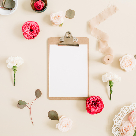 Flat lay floral frame with blank clipboard, red and beige rose flower buds, white carnation, eucalyptus, ribbon on pale beige pastel background. Top view decorated concept.の写真素材