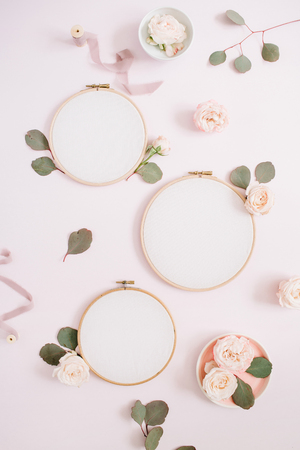 Embroidery frames with beige rose flower buds and eucalyptus on pale pastel pink background. Flat lay, top view decorated concept.の写真素材