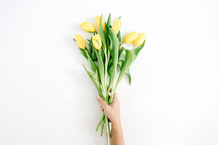 Girl's hands holding beautiful yellow tulip flowers bouquet on white background. Flat lay, top view.の写真素材