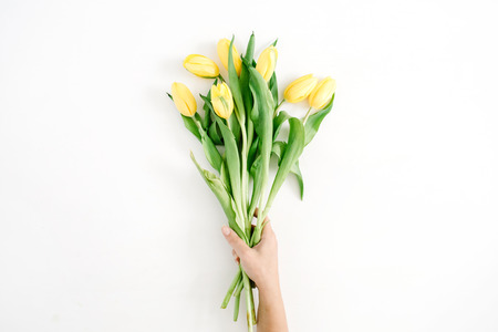 Female hand holding beautiful yellow tulip flowers bouquet on white background. Flat lay, top view.の写真素材