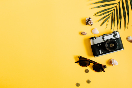 Flat lay traveler accessories on yellow background with palm leaf, camera and sunglasses. Top view travel or vacation concept. Summer background.の写真素材