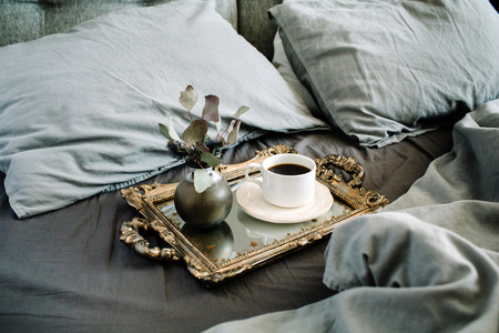 Morning coffee on golden vintage tray in bed with grey sheet and pillows.の写真素材