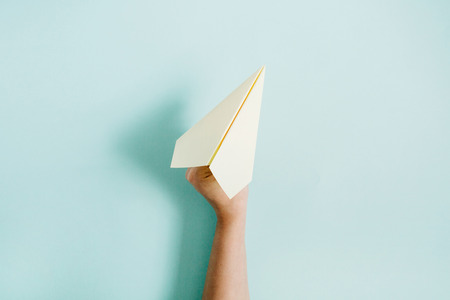 Women hand holding paper plane on pale blue background. Flat lay, top view.の写真素材