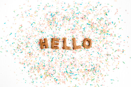 Word Hello made of sweet cookies letters on white background with colorful confetti. Flat lay, top view.の写真素材