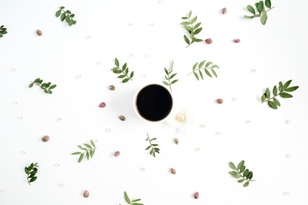 Floral pattern with coffee cup, flower buds, green leaves, branches on white background. Flat lay, top view.の写真素材